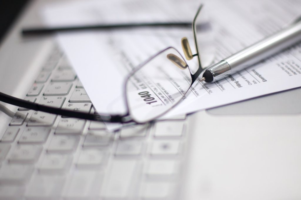Tax Season: Horizontal side view of an office laptop, eyeglasses with a metallic pen on an Income Tax Return Form as a reminder, digitally generated image copy space